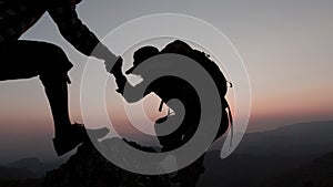 silhouette of Hikers climbing on rock, mountain at sunset, one of them giving hand and helping to climb. support, help and success