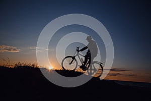 Silhouette of a hipster man on a bicycle on sunset background