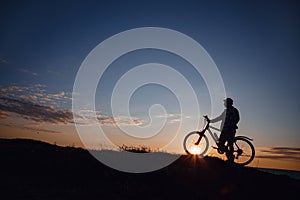 Silhouette of a hipster man on a bicycle on sunset background