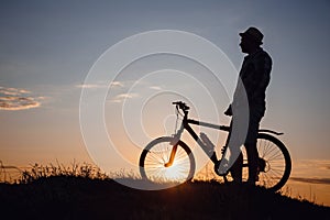 Silhouette of a hipster man on a bicycle on sunset background