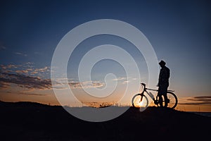 Silhouette of a hipster man on a bicycle on sunset background