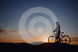 Silhouette of a hipster man on a bicycle on sunset background