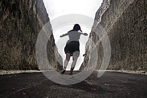 Silhouette on the horizon of young happy and active woman running and jumping excited on road between mountain cliffs feeling free