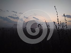 Silhouette of houses in the morning fog over a field with grass in autumn in nature