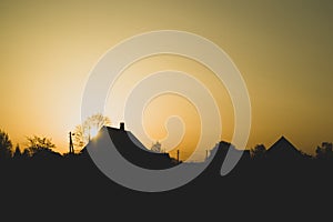 Silhouette of houses with trees at sunset. sun setting behind the forest