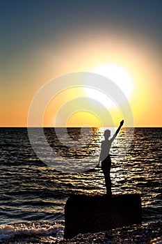 Silhouette of a human figure on the background of the sunset over the sea. A man stands on a large rock, on which the sea waves br