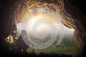 Silhouette humble man sitting on a rock in cave looking at birds