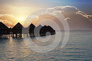 Silhouette hut over the transparent quiet sea water on a sunset. Maldives