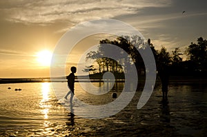 Silhouette image a boy playing beach football over sunrise background