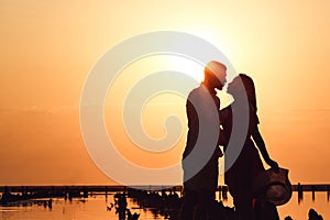 Silhouette image of a loving couple embracing at sunset on a lake.