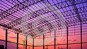 Silhouette of incomplete factory building structure with curve metal roof beam against colorful twilight sky