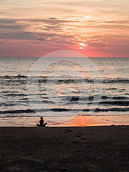 Silhouette of an indefinite person in lotus position on a sea sandy beach during a beautiful sunset. Meditation during sunset. A