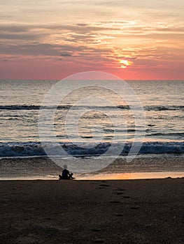 Silhouette of an indefinite person in lotus position on a sea sandy beach during a beautiful sunset. Meditation during sunset. A