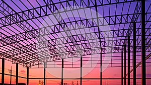 Silhouette industrial building structure with curved roof beam and column in construction site against colorful twilight sky