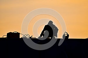 Silhouette of an industrial professional welder welding huge steel structure of gantry crane at seaport.