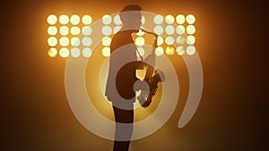 Silhouette jazz musician playing saxophone in spotlights. Man performing melody.