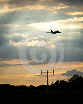 Silhouette of jumbo jet flying at sunset behind high tech radio mast for communications between pilot and airport