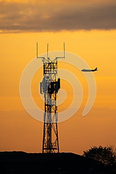 Silhouette jumbo jet flying sunset behind high tech radio mast for communications between pilot and airport. Air traffic control