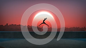 Silhouette of jumping ballet woman with skyline of skyscraper city in the background. Sunset with large sun.