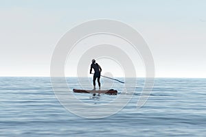 Silhouette of a kayaker on a personal rowing kayak, rowing a kayak with an oar in the sea at dawn