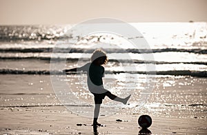 Silhouette of the kid boy play football on the beach with a ball. Summer soccer on beach for children.