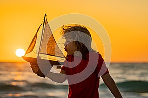 Silhouette of kid playing with toy seailing boat on sunset sea. Child boy play on the beach on a sunny day. Little