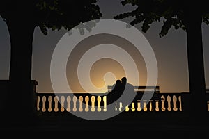 Silhouette of a kissing couple in love on a sunset background. Palm trees and a bench. Sea view point. Vacation and tourism