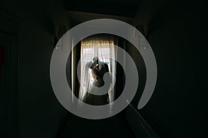 The silhouette of the kissing newlywed couple standing near the window in the dark room.