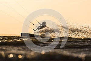 Silhouette of Kitesurfer riding in sunset conditions with backlit spray of water