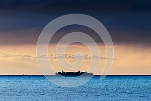 Silhouette of large container ship crossing Baltic sea under dramatic dark nimbostratus cloud formation.