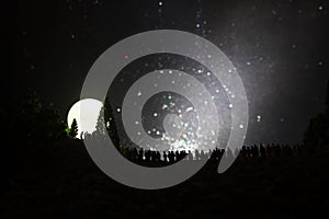 Silhouette of a large crowd of people in forest at night watching at rising big full Moon. Decorated background with night sky wit