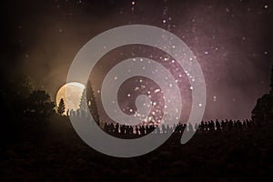 Silhouette of a large crowd of people in forest at night watching at rising big full Moon. Decorated background with night sky wit