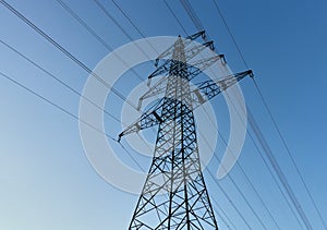 Silhouette of a large electricity pylon against the blue sky