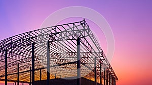 Silhouette of large factory building structure in construction site against colorful twilight sky background, low angle view