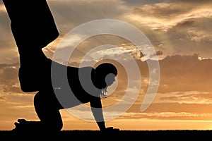 Silhouette of a large man`s leg presses on a woman standing on all fours