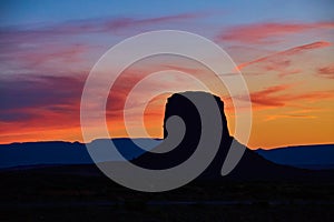 Silhouette of large red rock pillar in desert against sunset sunrise at Monument Valley