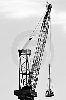 Silhouette of a large tower crane lifting construction workers