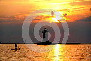 Silhouette of a light house and a man on a paddle board during sunset at Cape Henlopen State Park, Lewes, Delaware, U.S.A photo
