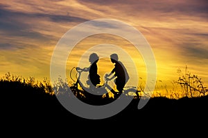 Silhouette little boy and little girl riding bike on sunset