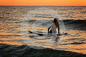 Silhouette of a little boy servere waiting for waves at sunset