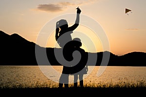 Silhouette of little daughter and mother playing a kite by the lake at sunset. Healthy summer activity for children. Funny time