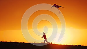 Silhouette of little girl launch kite, running on meadow at golden sunset