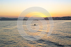 Silhouette of a lone canoeist paddling in Santos Bay during sunset