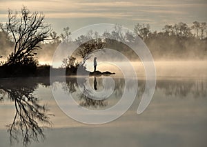 Silhouette of a lone figure standing by a misty lake