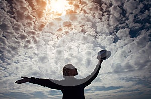 Silhouette of lonely happy traveler woman with open outstretched arms against beautiful cloudy sky. Freedom concept and enjoying