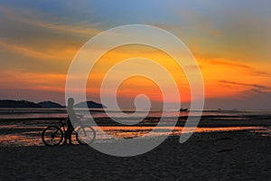 Silhouette of lonely unidentified girl with bike on beach with sunset light