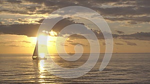 Silhouette of lonely yacht sailing in ocean waves. Lonely sailboat drifting at golden sunset horison at open sea