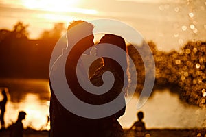 Silhouette of loving couple hugging on the lake at sunset. Beautiful young couple in love walking on the shore of the lake at