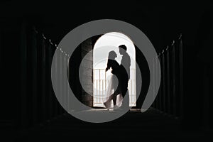 Silhouette of loving couple hugging while standing in doorway on black background, Bride and groom in wedding day posing in a