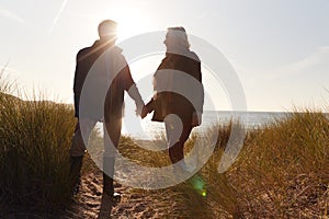 Silhouette Of Loving Senior Couple Holding Hands As They Walk Along Coast Path Against Flaring Sun